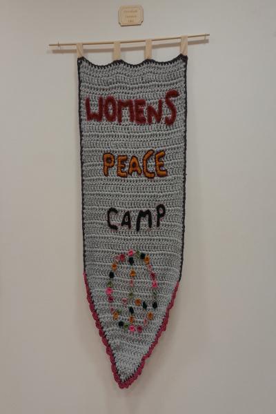 A textile banner with the words Women's Peace Camp and a colourful peace symbol below.