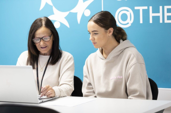 teacher helping student at a laptop
