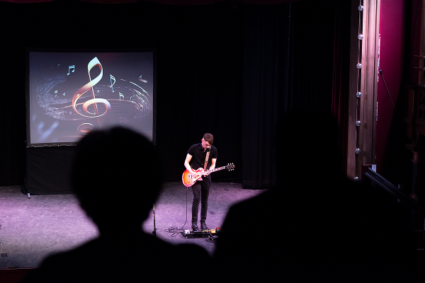 Applicant performing on stage with a guitar
