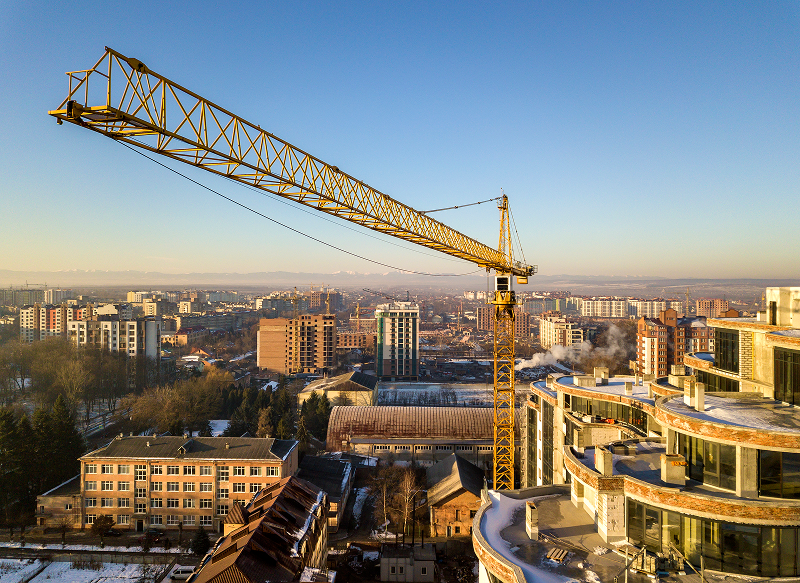 Yellow construction crane over a cityscape with modern buildings under a clear blue sky