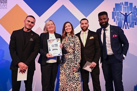Group photo at the &#039;WORKER OF THE YEAR AWARDS&#039; with one person holding a framed certificate in front of a colourful backdrop
